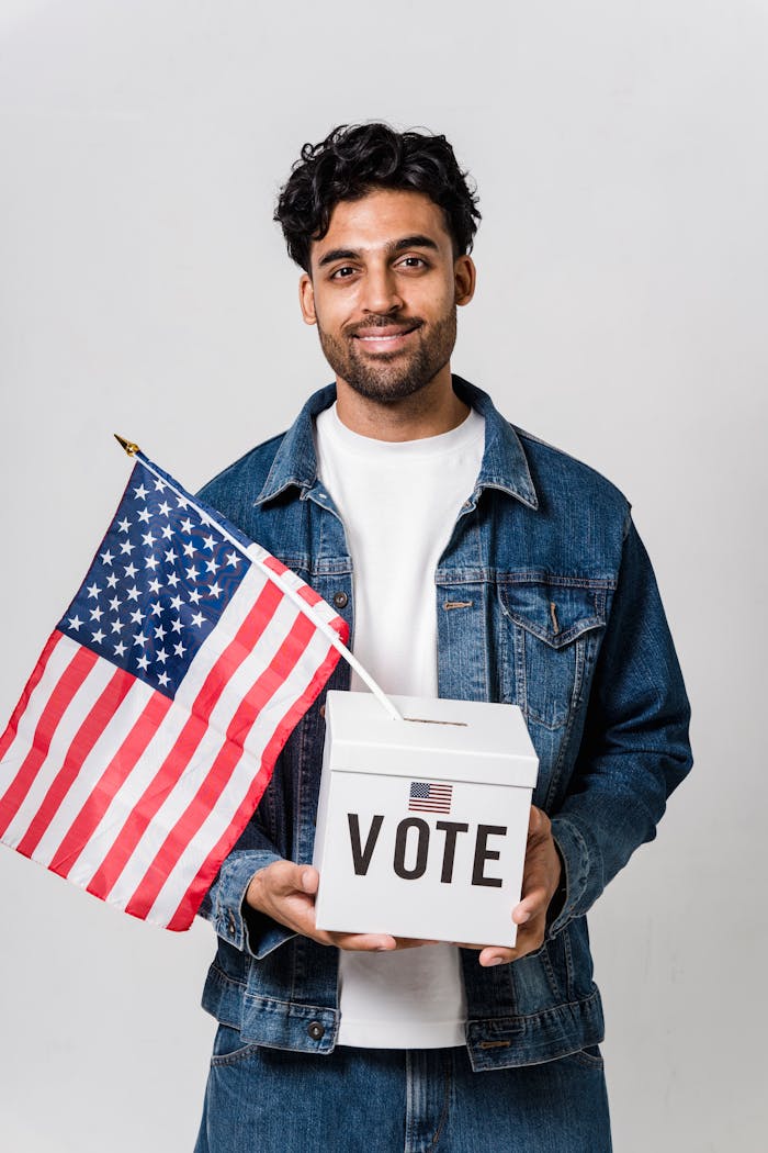 hero-img-01 Young man in denim holding a vote box and American flag, studio shot.